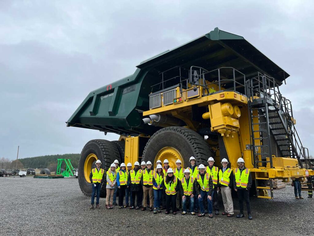 A group of students in the Student Leadership Council poses for a photo in front of a large mining vehicle during a cohort trip to Seattle in March 2024.