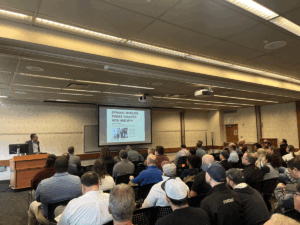 Professor Aliprantis presenting in front of an audience at the Purdue Road school presentation on March 19, 2025.