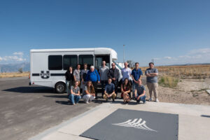 ASPIRE students and faculty pose for a group photo outside of the ASPIRE mini bus in front of the 1 MW DWPT charger at the Utah Inland Port.