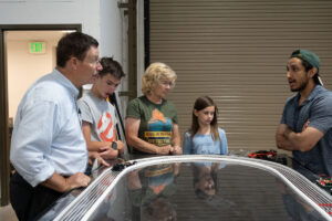 Family gathers around a model EV track as ASPIRE student explains what is occuring.