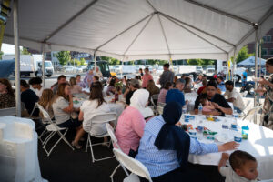 People gather under the white canopy to eat a delicious dinner of pulled pork/chicken sandwiches.