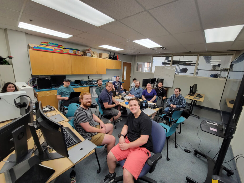 Group of USU ASPIRE students pose for a photo from their desks at the annual USU Hackathon event.