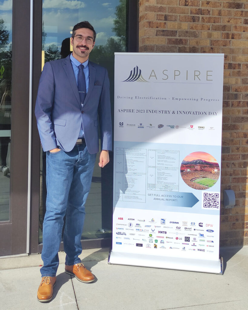 Mahyar Vahedi Saheli standing next to an ASPIRE Industry and Innovation Day pop-up poster.