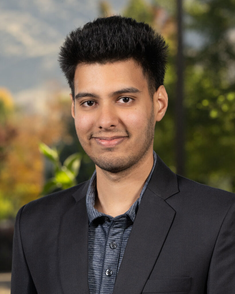 Sanat Poddar smiles into the camera against a blurred background.
