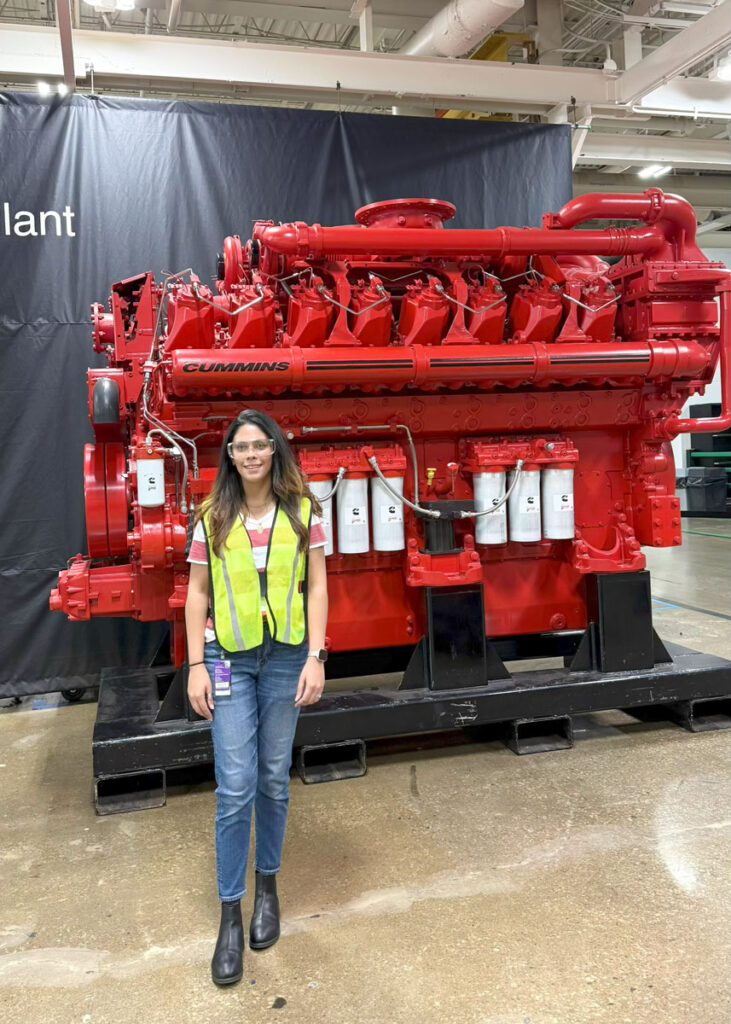 Zainab Imram smiles in front of red equipment at her internships at Cummins.