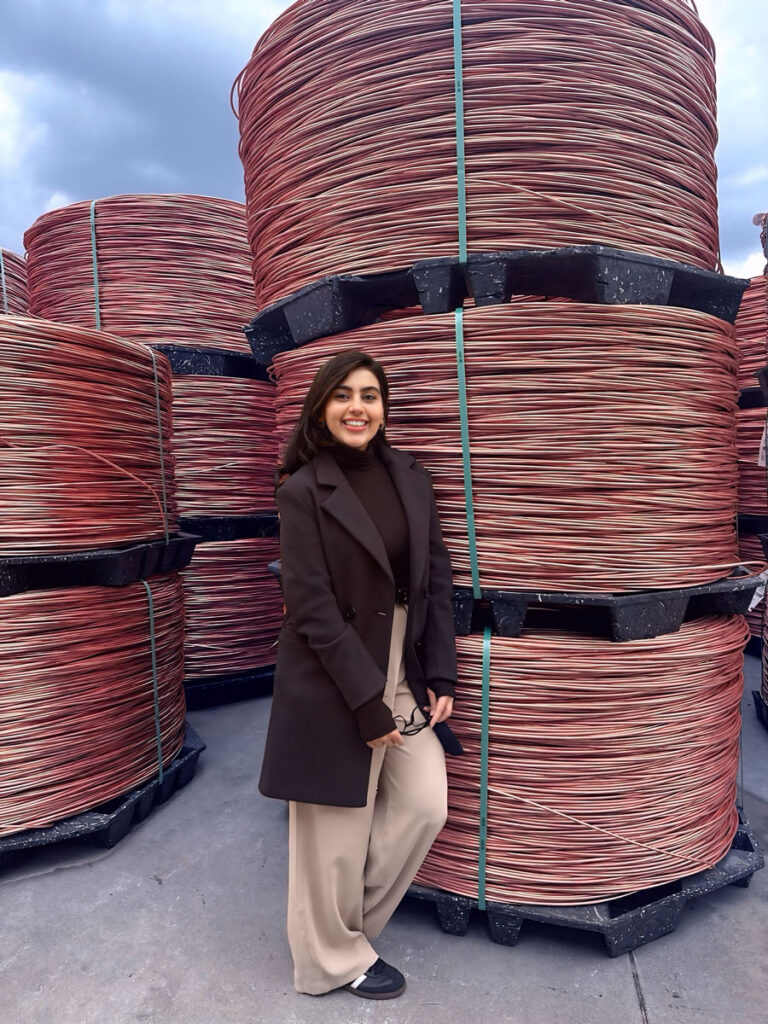 Sarah Sami Khan standing next to giant spools of copper rods.
