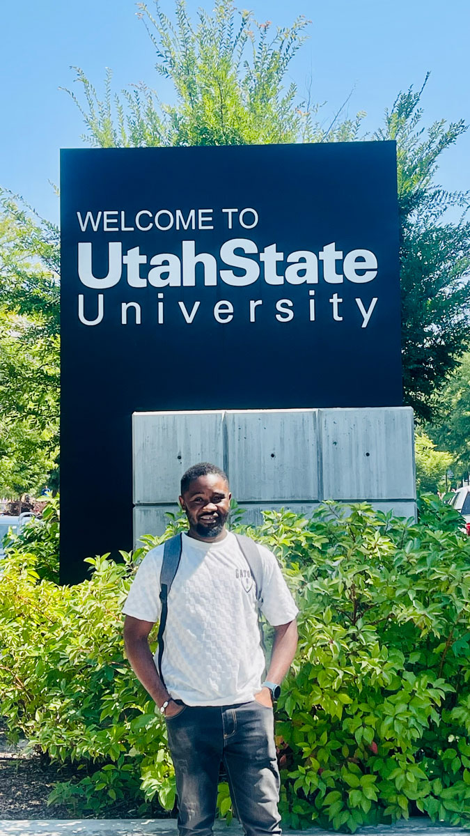 Foeday Zinnah in front of a Welcome to Utah State University sign.