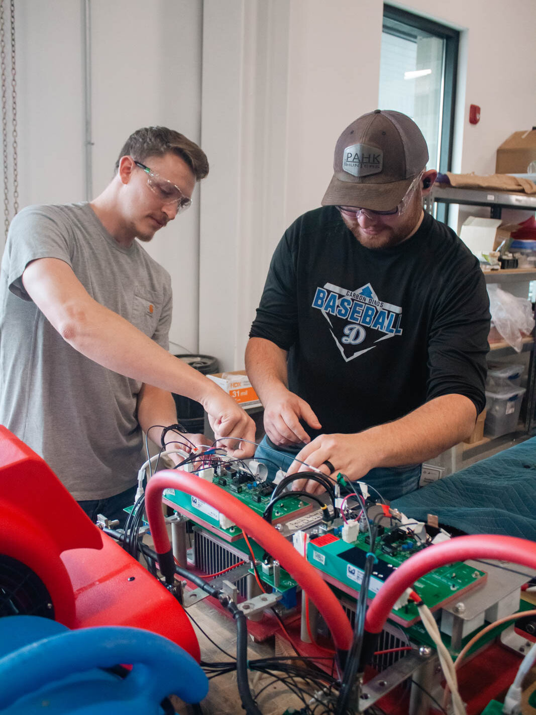 An engineering student works on wiring for an electric vehicle system component under supervision.