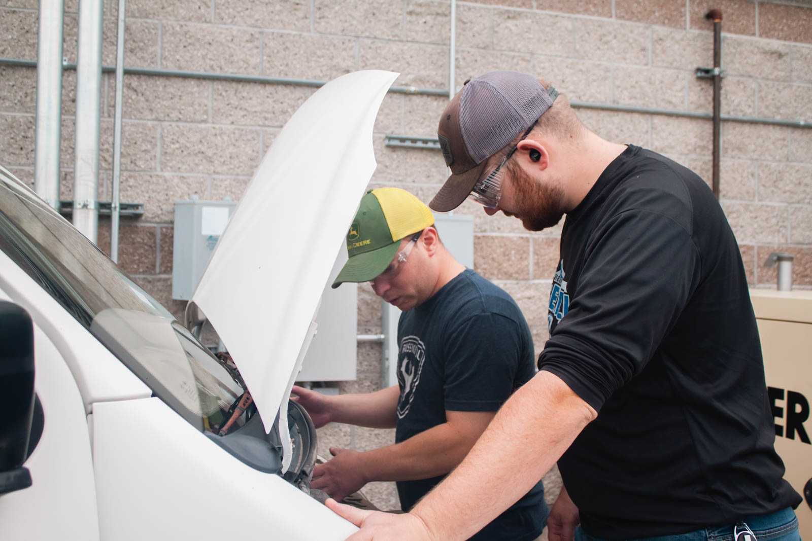 Two engineering students work under the hood of an electric kit car.