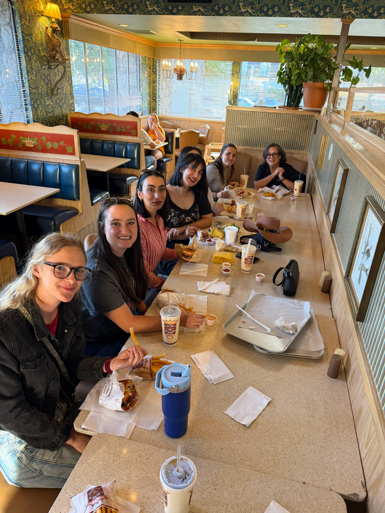 ASPIRE Student Leadership Retreat participants enjoy lunch together at a long restaurant table, with food trays, drinks, and booth seating visible throughout the dining area.